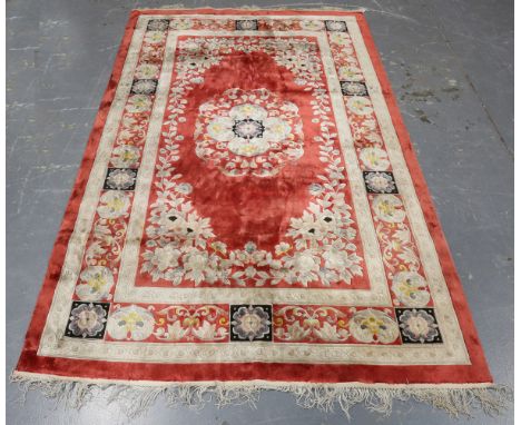 A Chinese part silk rug, late 20th century, the red field with a scroll medallion, within a palmette and scroll border, 241cm