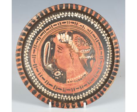 A Greek Apulian black glazed red figure footed plate, 4th century BC, decorated with a central profile portrait of a lady, di