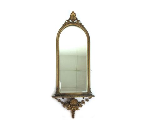 A early 19th century gilt wood rococo style mirror, with shell carving over arched topped beveled glass above a shaped shelf 