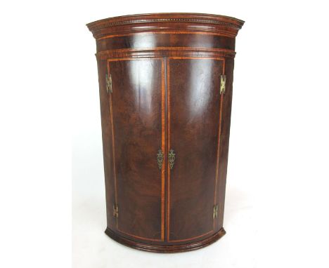 A late 18th century and later mahogany and satinwood banded bow front corner cupboard, the double doors opening to reveal thr