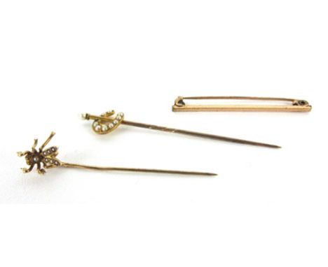 A yellow metal stick pin in the form of a winged insect and set seed pearls, together with another in the form of a horseshoe