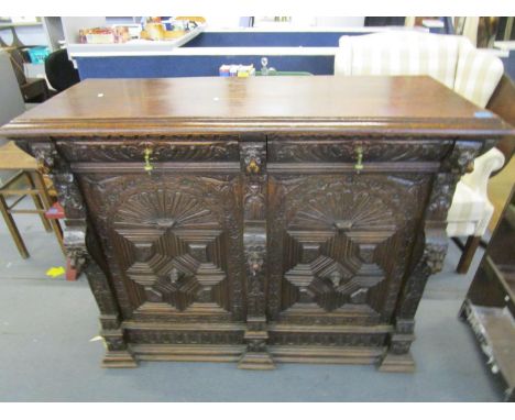 A Victorian carved pussy oak side cabinet, two drawers with brass drop handles over two cupboard doors on a stepped block fee