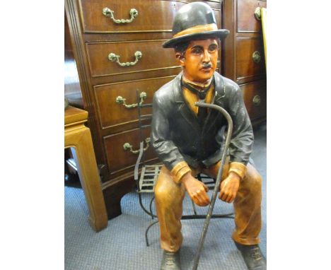 A painted composition model of Charlie Chaplin, sitting on a metal chair 