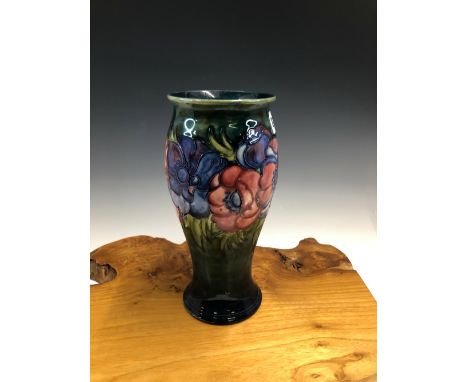 A WILLIAM MOORCROFT PEONY PATTERN BALUSTER VASE, THE FLOWER HEADS SLIP TRAILED ONTO A BLUE/GREEN GROUND.   25.5cms.