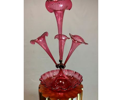 A LATE VICT0RIAN CRANBERRY GLASS EPERGNE, THE CENTRAL TRUMPET VASE FLANKED BY THREE SMALLER, ALL SUPPORTED ON A WAVY EDGED CI