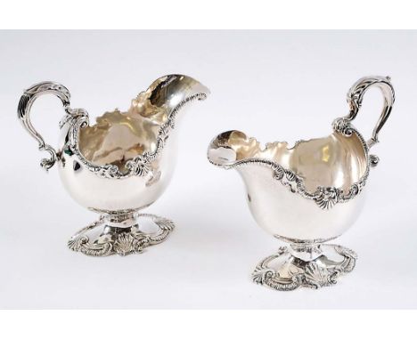 A PAIR OF GEORGE II SAUCE BOATS of bellied form on shaped pedestal bases with cast borders of gadrooned scrolls & shells, lea