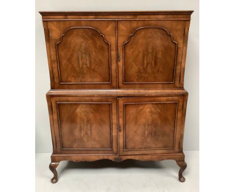 A 20th century walnut drinks cabinet, two panelled cupboard doors enclosing a shelf, above another pair of cupboard doors enc