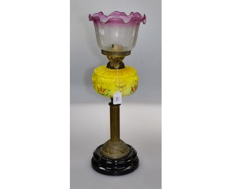 A late Victorian paraffin table lamp, having a cranberry tinted and etched shade over yellow painted, florally moulded reserv