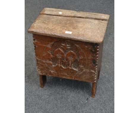 An 18th century oak hearth box stool, the hinged lid over carved front decorated with twin stylised half moons on shaped end 
