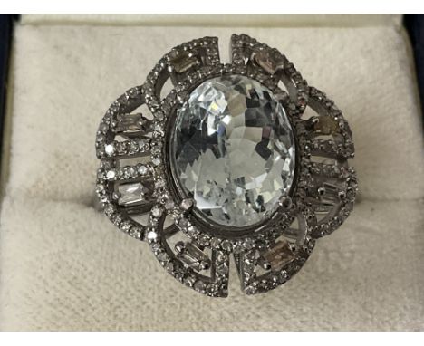 Ornate dress ring in silver, set with an oval aquamarine surrounded by baguette and R/C diamonds in a filigree mount, boxed. 