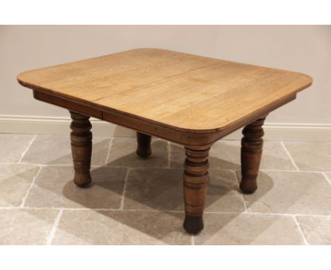 A late Victorian honey oak extending dining table, the rectangular top with rounded corners raised upon substantial ring turn