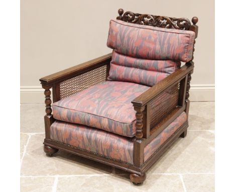 An early 20th century oak bergere armchair, later re-covered in Liberty style fabric, the scrolling foliate openwork pediment