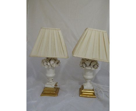 A pair of Belleek style lamps with central ceramic campana urn with fruit and foliage, raised on square wooden bases and ivor