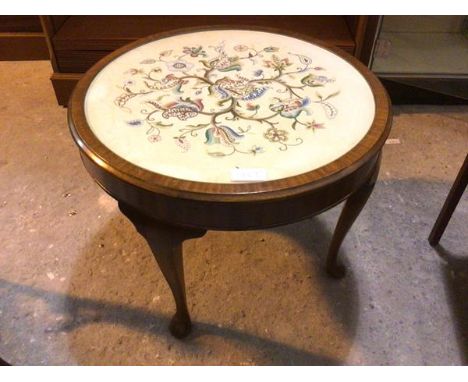 A 1930s circular mahogany occasional table with floral embroidered top under glass, on four cabriole supports ending in pad f