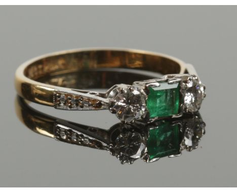 An 18ct gold and platinum three stone emerald and diamond ring. Square cut emerald flanked by a pair of brilliant cut diamond