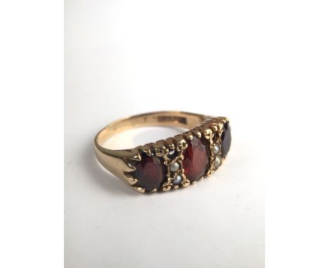 A Victorian 9ct gold and split pearl ring set with three oval free cut red garnets with seed pearl accent (Two vacant pearls)