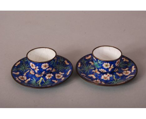Pair of C18th/19th Chinese painted enamel cups and saucers, painted with bamboo and prunus in a blue ground, the saucers 11.2