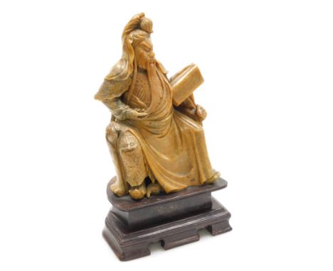 A Chinese soapstone figure of Guan Yu, Chinese god of wealth, modelled seated on a throne, with a scroll, raised on plinth ba