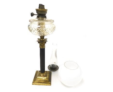 An early 20thC brass Corinthian column table lamp, with a faceted cut glass reservoir, glass chimney and white globe form sha