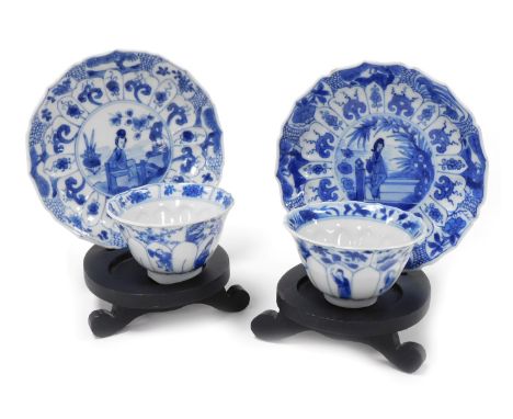 A pair of Kangxi porcelain blue and white tea bowls and saucers, of moulded floral form, decorated with figures beneath bloss