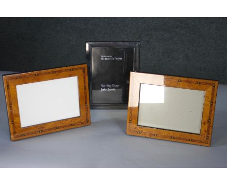 A John Lewis sterling silver easel picture frame along with a pair of marquetry inlaid veneered portrait picture frames. L.23