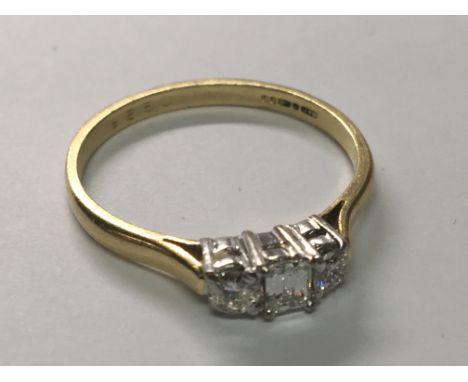 An 18carat Yellow gold diamond ring with a central emerald cut diamond flanked by brilliant cut diamonds the diamond of excel