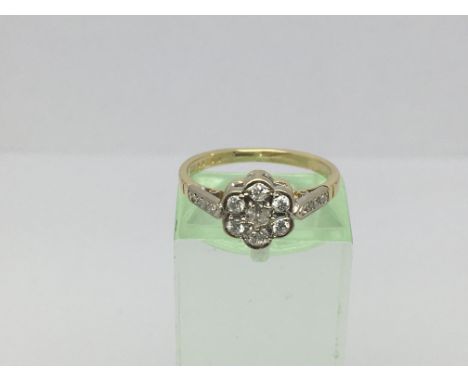 An 18ct gold and platinum ring set with seven diamonds in a rose setting with further diamonds to the shoulders, approx 2.7g 