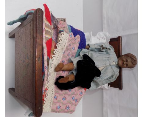A male doll with carved head and lower limbs with a fabric torso, together with a wood bed and vintage covers.