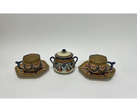 A pair of French Quimper faience hexagonal teacups and saucers decorated with circular garlands on orange ground (marked vers