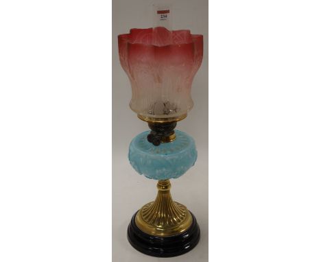 A Victorian pedestal oil lamp, having a cranberry tinted frilled glass shade above a blue glass font, on a brass pedestal bas