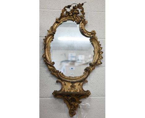 An antique rococo style mirror with giltwood and gesso floral and foliate frame and integrated shelf a/f, 86 x 50 cm