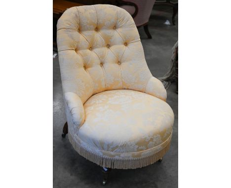 A Victorian walnut framed nursing chair upholstered in yellow floral button back fabric, turned front legs and brass casters