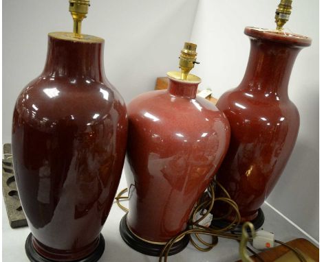 A selection of three red ceramic table lamps, of various sizes and designs, each raised on a stained wood circular base, the 