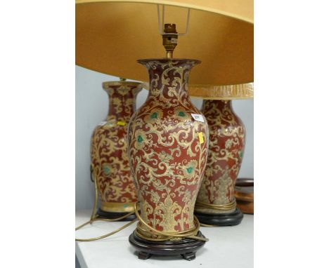 A pair of 20th Century ceramic table lamps, decorated with stylized scrolling foliage on an enamelled red ground, each on a s