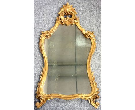 19th Century wall mirror with a shaped upright plate, in a carved floral and scroll gilt frame, 110.5 x 59cm overall 