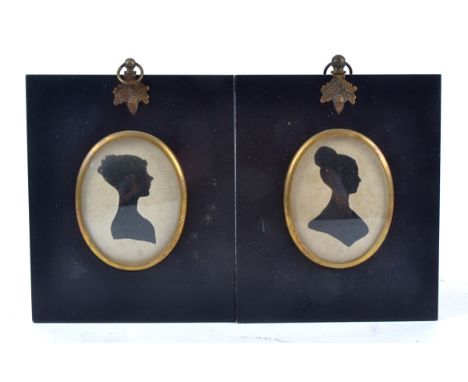 A companion pair of oval silhouette portrait miniatures of Georgian ladies, in ebonised frames, hanging from gilt acorns and 