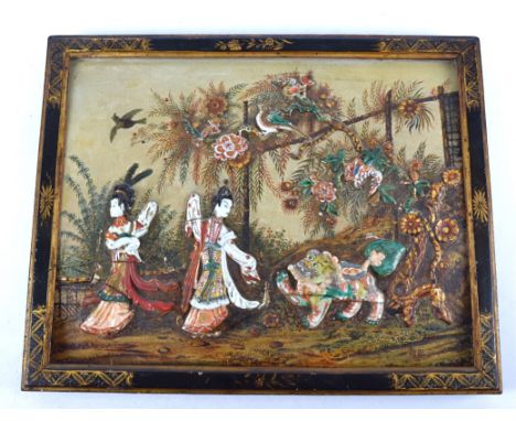 An oriental carved wooden plaque, depicting two figures and a guardian lion in ceramic, underneath a blossoming tree, all pai