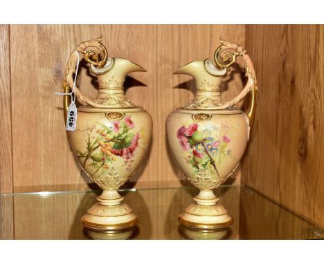 A PAIR OF ROYAL WORCESTER BLUSH IVORY EWERS, florally decorated with gilt detailing, the body raised on stepped circular plin