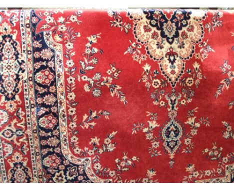 A Persian style red ground carpet with traditional lozenge shaped centre, further abstract floral decoration  and set within 