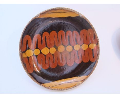 A St Ives pottery dish by Bernard Leach with slipware decoration in dark brown, brick red and ochre incorporating a wavy line