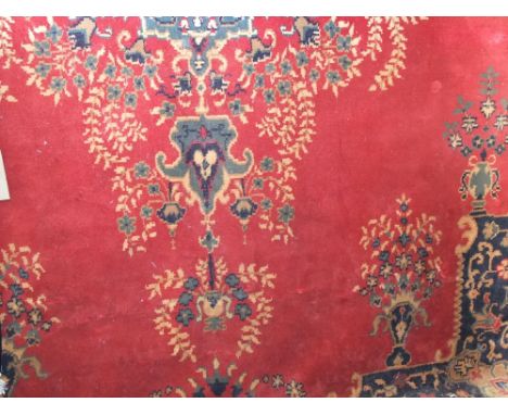A Persian style wool carpet with medium ground red field, central medallion with further floral bouquet detail within wide ru