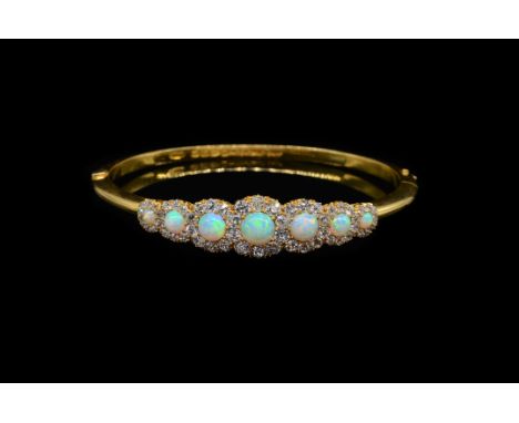 A VICTORIAN OPAL AND DIAMOND BANGLESet with seven cabochon opals, each surrounded by a halo of old cut diamonds, on a hinged 