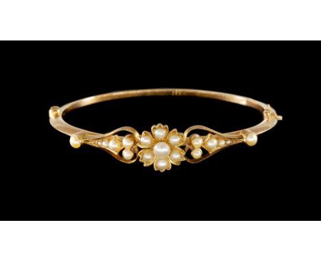 AN EDWARDIAN SEED PEARL BANGLEWith a flowerhead shaped motif at the centre, on a snap clasp, indistinctly detailed 15, circa 