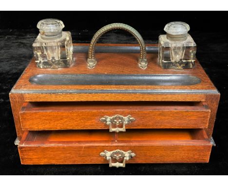 A large late Victorian oak inkstand, arched carrying handle flanked by a pair of square glass wells, above two long drawers, 