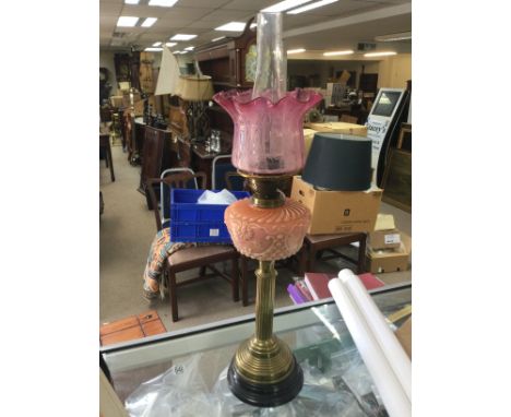 A Victorian brass oil lamp with a pink reservoir and a cranberry glass shade.