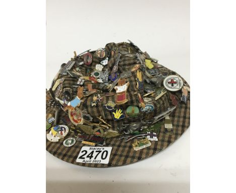 A large quantity of vintage enamel badges mounted on a hat.