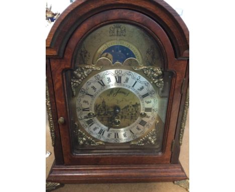 A Reproduction mahogany manual clock the arched dial with Roman numerals.
