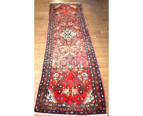 An Iranian red ground wool runner carpet. With multi borders, floral central medallion, 300cm x 82cm