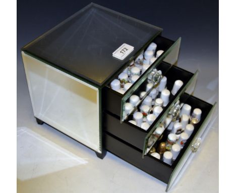 A mirrored three drawer jewellery box enclosing a collection of ceramic thimbles