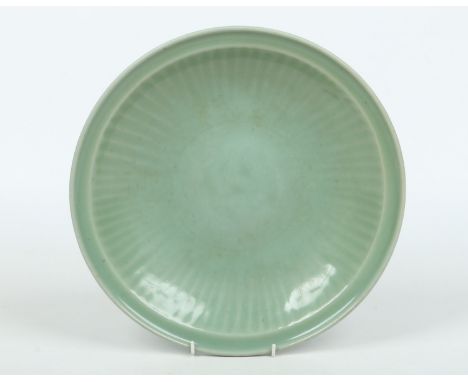 An antique Chinese heavily potted celadon glazed dish with light fluted moulding to the well, 34.5cm diameter.  Condition Rep